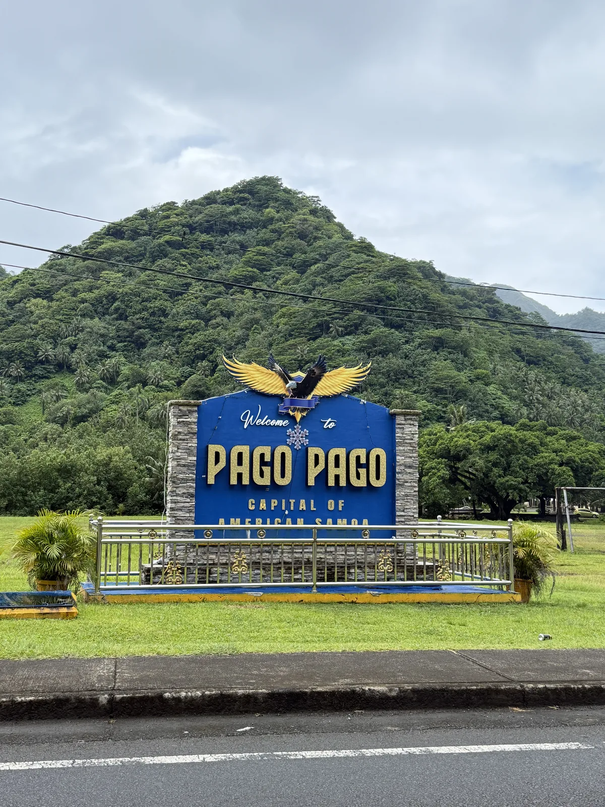 Cartel de bienvenida a Pago Pago ante una montaña cubierta de vegetación